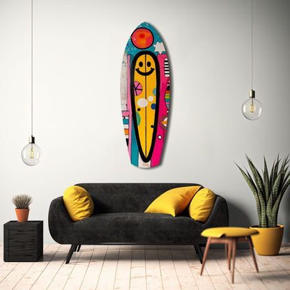 Colorful smiley surfboard wall art displayed above black sofa with yellow pillows in modern living room setting.