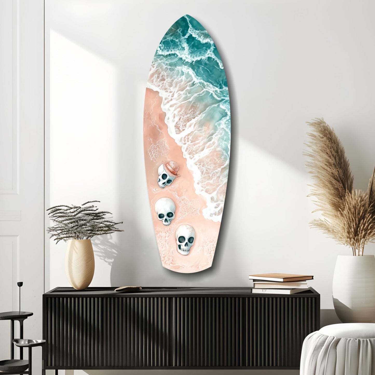 Surfboard-shaped glass wall art featuring aerial ocean waves in teal and white with three skull designs on sandy beach, displayed above black cabinet.