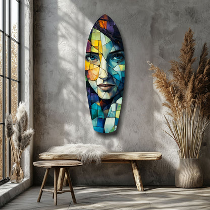 Colorful stained-glass style portrait of a woman's face mounted on a textured gray wall above wooden furniture and dried pampas grass.