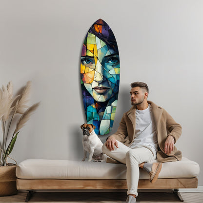 Man sitting on wooden bench beside colorful stained-glass style surfboard wall art featuring abstract female face with vibrant geometric patterns.