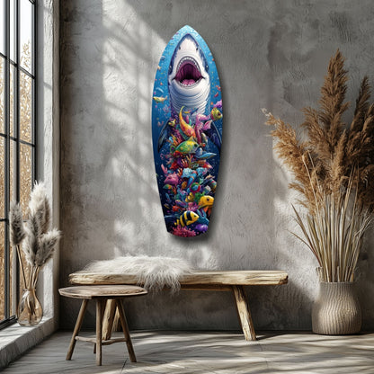 Surfboard-shaped glass wall art featuring a great white shark with open mouth above colorful coral reef fish, displayed on gray wall above wooden bench.