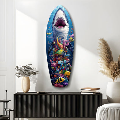 Shark-shaped glass wall art displaying a great white shark with open mouth above colorful coral reef fish, mounted above a black cabinet in a minimalist interior.
