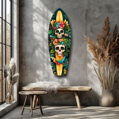 Coffin-shaped glass wall art featuring two skulls adorned with colorful flowers and a yellow candle, displayed above a wooden bench in a minimalist room.