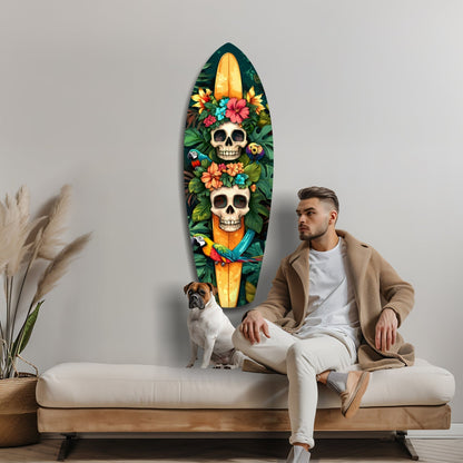 Man sitting on cream bench beside surfboard-shaped glass wall art featuring two skulls surrounded by colorful flowers and tropical birds on dark background.