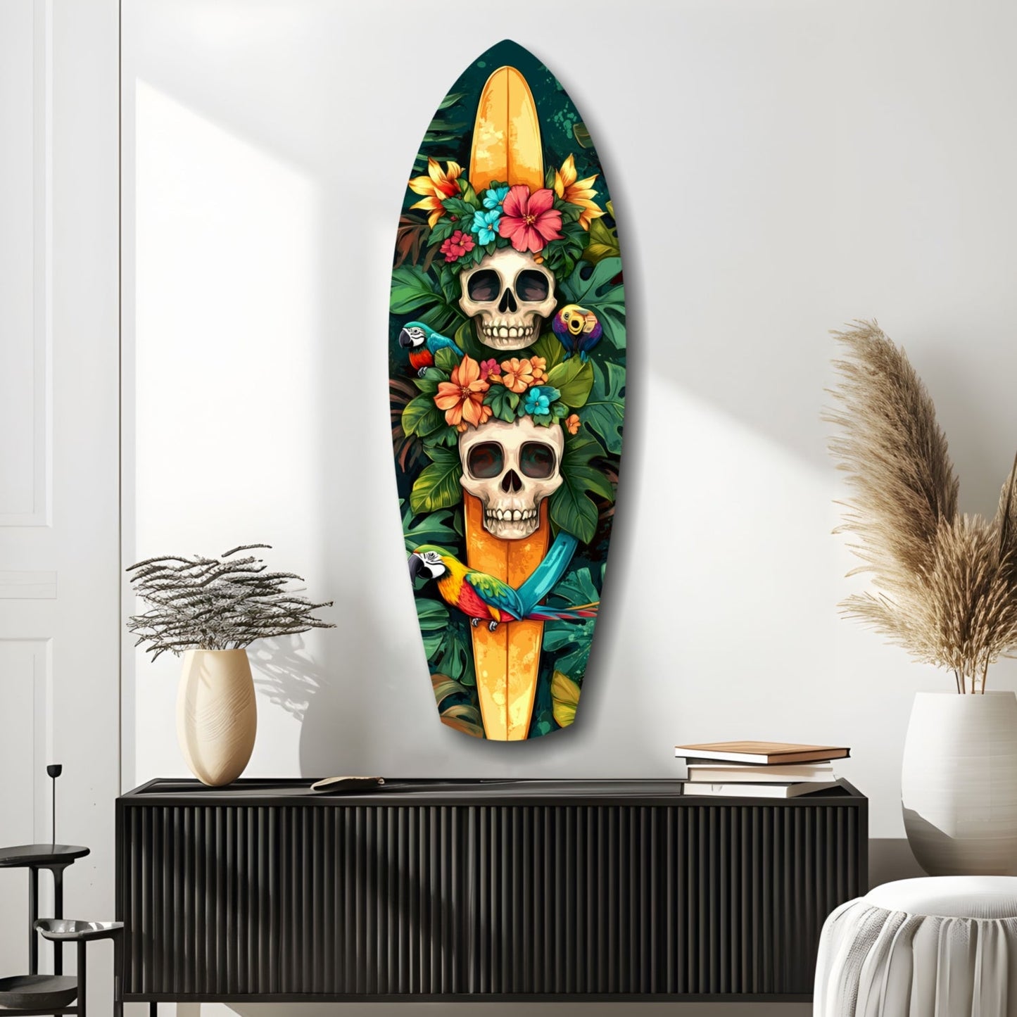 Surfboard-shaped glass wall art featuring two skulls adorned with colorful tropical flowers, parrots, and foliage on dark background, displayed above black cabinet in modern room setting.