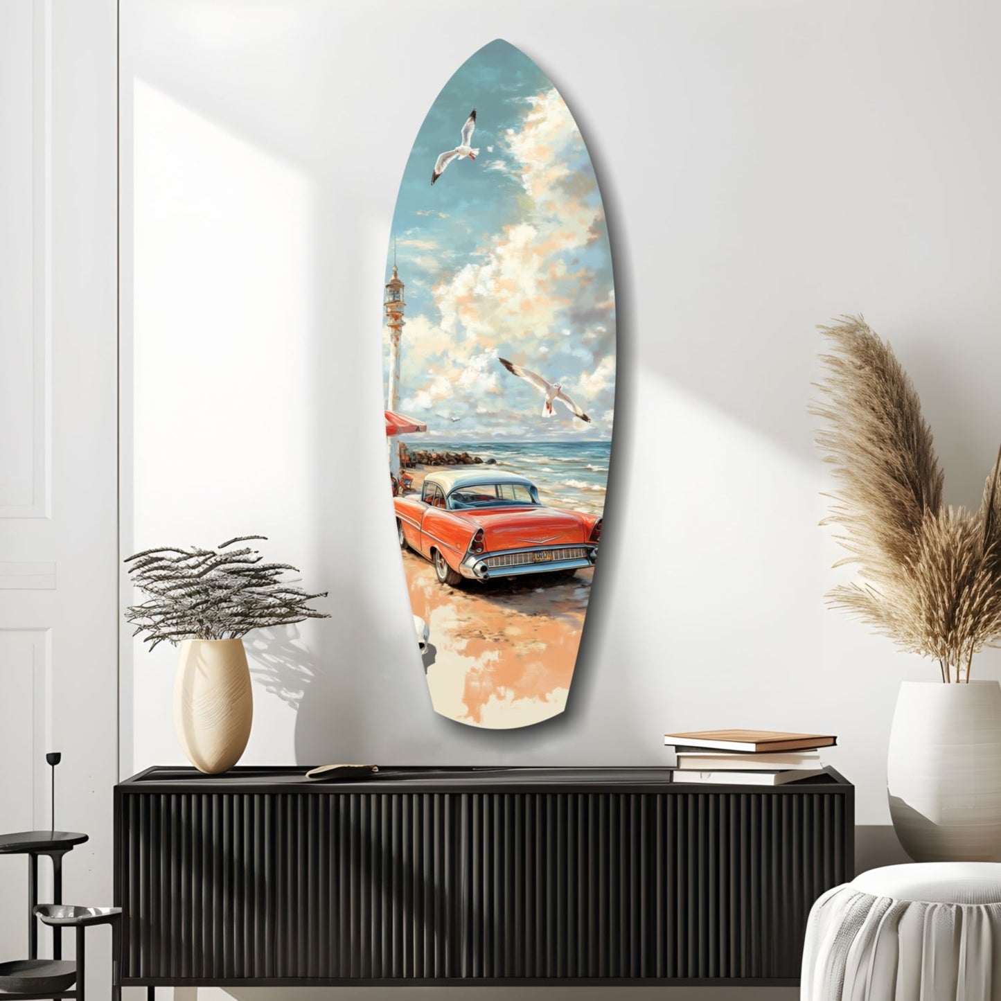 Surfboard-shaped glass wall art depicting a red vintage car on a beach with lighthouse, seagulls, and blue sky, displayed above a black cabinet.