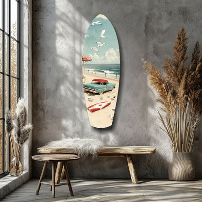 Surfboard-shaped glass wall art depicting a vintage beach scene with turquoise car, red umbrella, and sailboat, displayed above wooden bench in modern interior.