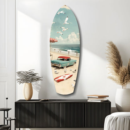 Surfboard-shaped glass wall art depicting a vintage beach scene with turquoise car, red umbrella, boats, and seagulls against white wall.