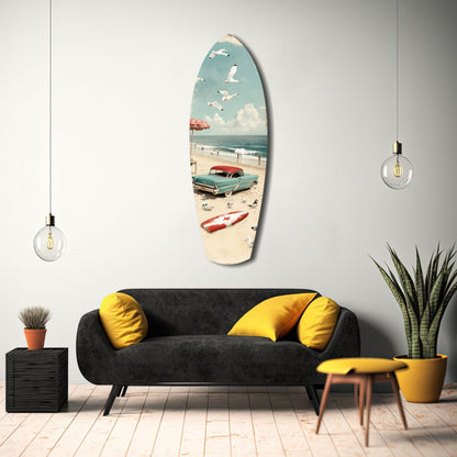 Surfboard-shaped glass wall art displaying vintage beach scene with turquoise car, sailboat, and seabirds, mounted above black sofa with yellow pillows.