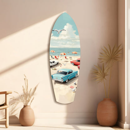 Surfboard-shaped glass wall art featuring a vintage beach scene with turquoise car, umbrellas, and seagull, displayed on beige wall beside terracotta vases.