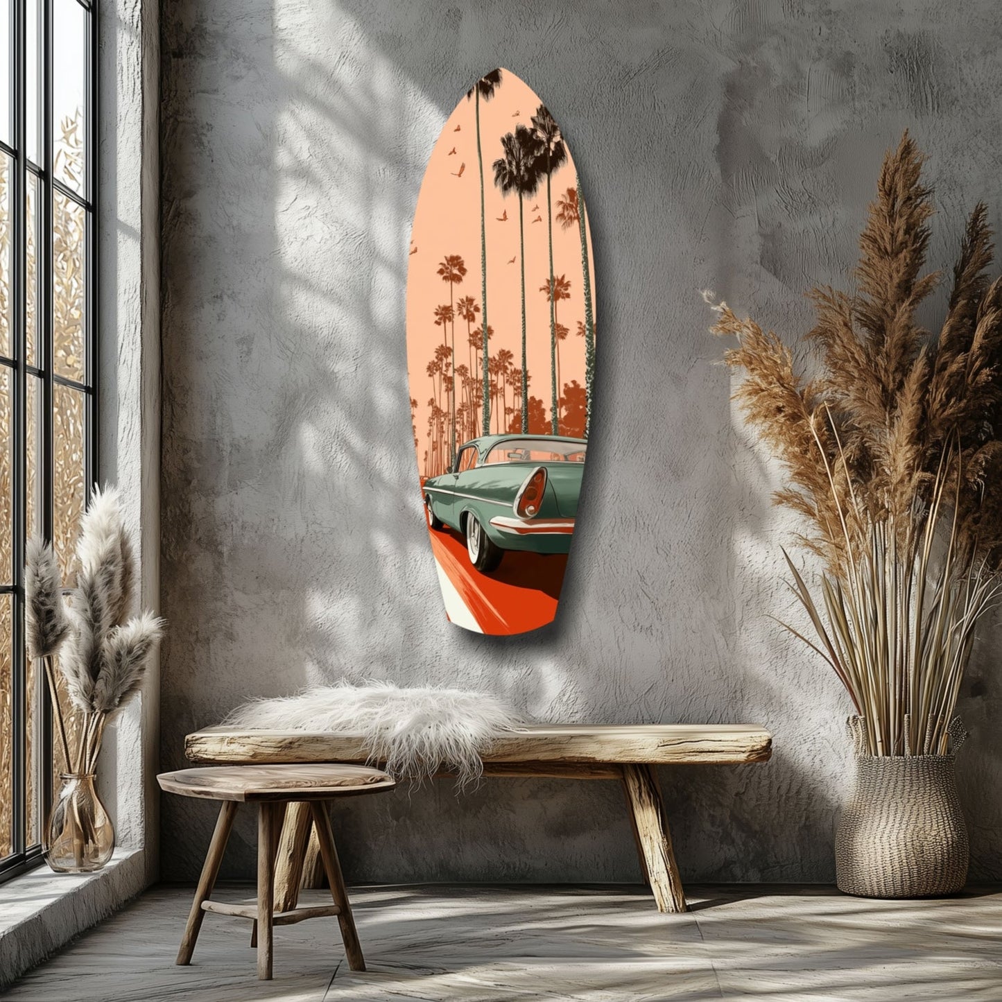 Surfboard-shaped glass wall art depicting a vintage green car on a coastal road with palm trees against a peachy sunset sky, mounted on a textured gray wall beside wooden furniture.