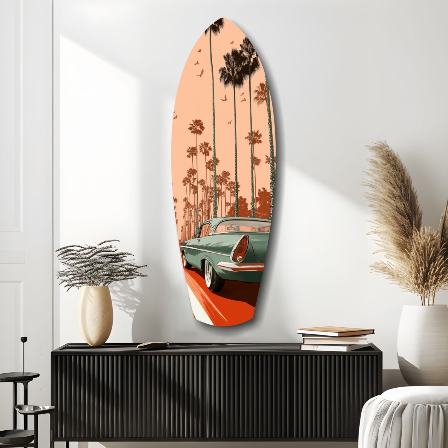 Surfboard-shaped glass wall art featuring a vintage green and red car beneath palm trees against a peachy-orange sky, displayed above a black ribbed cabinet.