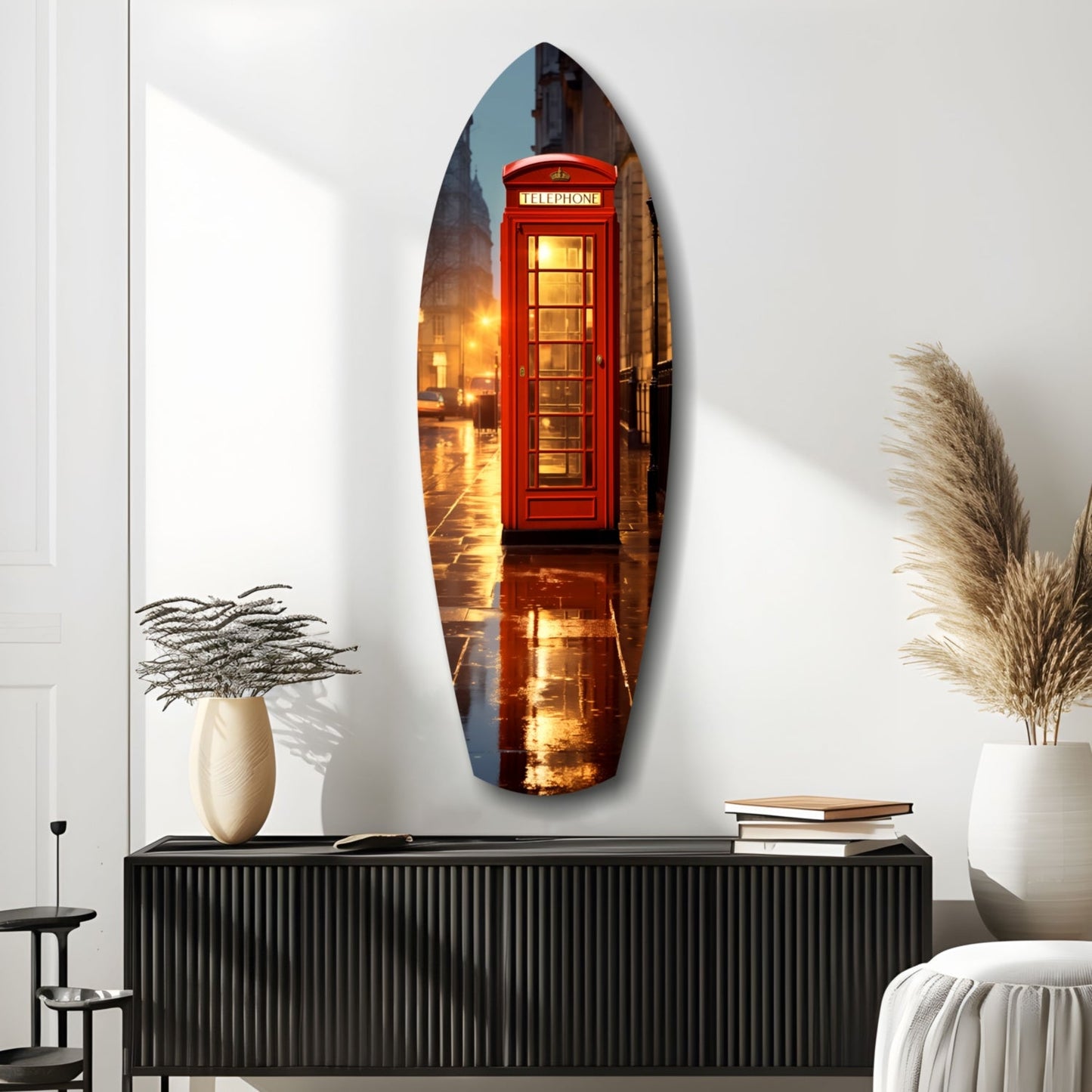 Oval glass wall art depicting a red British telephone booth illuminated at dusk on a wet street, displayed above a black ribbed console table.