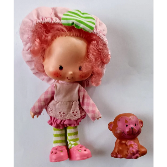 Vintage Strawberry Shortcake doll in pink dress and green hat holding monkey