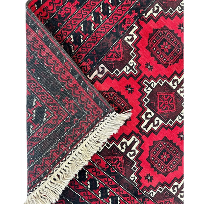 Vibrant Afghani Baluch wool rug with red black geometric patterns and cream fringe