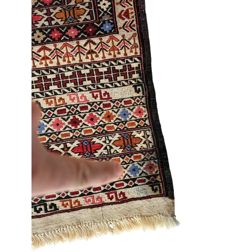 Hand touching bold geometric border of Afghani Maliki Soumak rug
