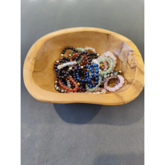 Vibrant stone ring collection with colorful beaded bracelets in wooden bowl