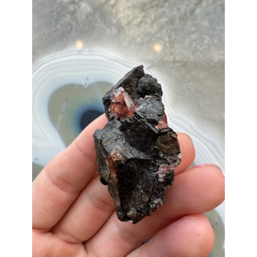 Hand holding stunning Brazilian Rhodochrosite crystal cluster on dark matrix