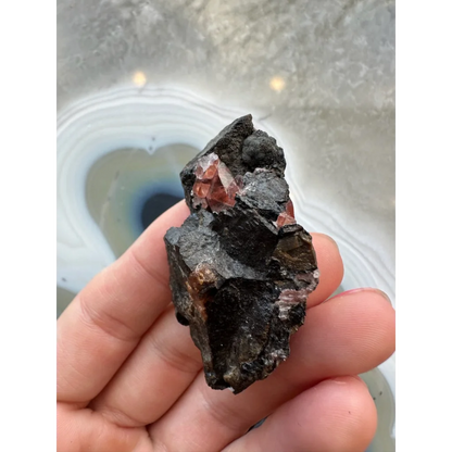 Hand holding stunning Brazilian Rhodochrosite crystal cluster on dark matrix