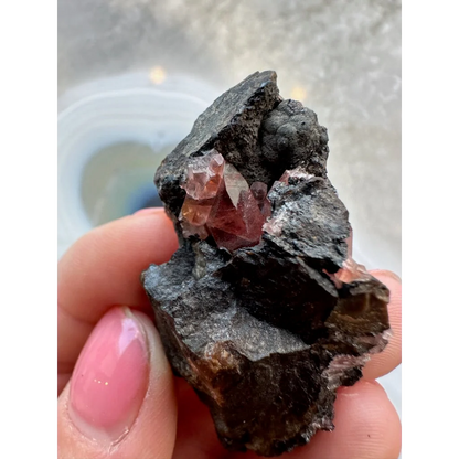 Hand holding stunning Brazilian Rhodochrosite crystal cluster on dark matrix