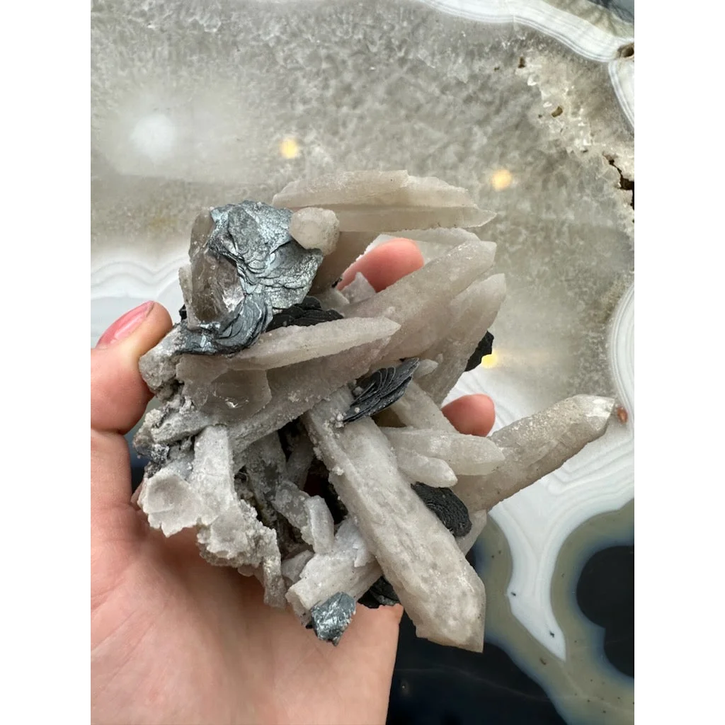 Hand holding dogtooth calcite with mica flakes and quartz crystals