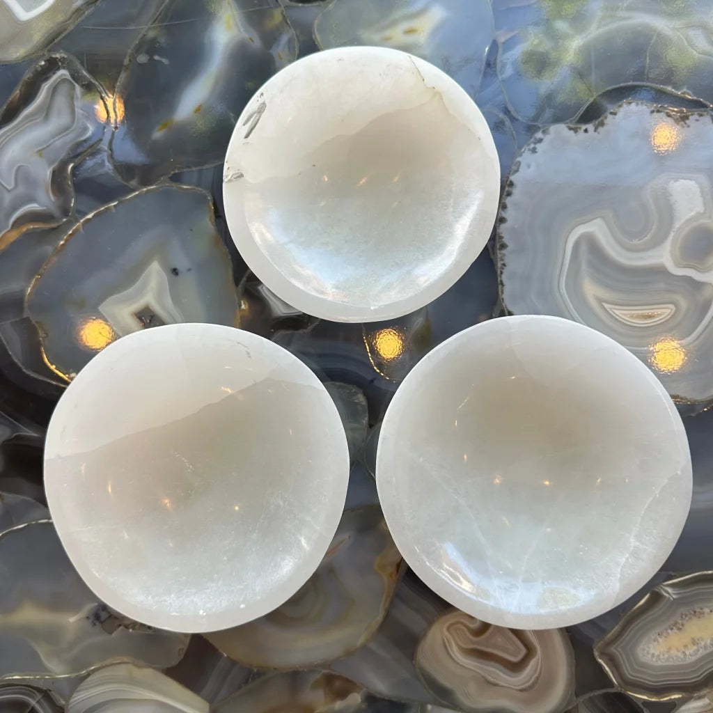 Three translucent white selenite bowls on agate surface