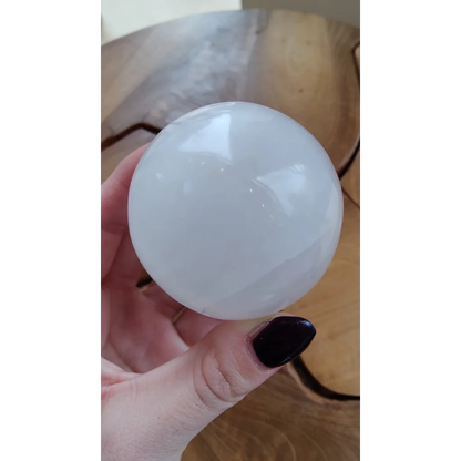Hand holding smooth translucent white selenite sphere
