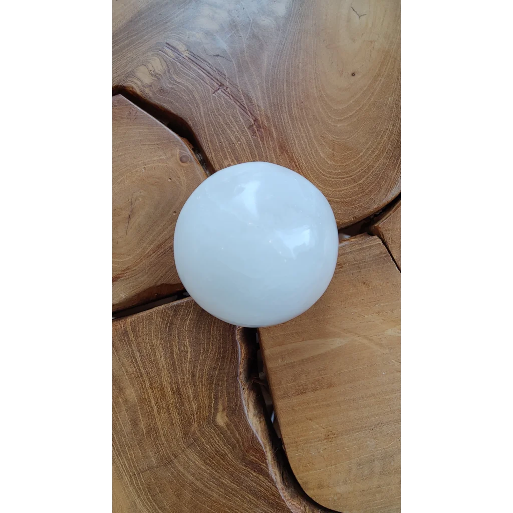 Smooth white selenite sphere on rustic wood surface
