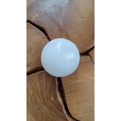 Smooth white selenite sphere on rustic wood surface