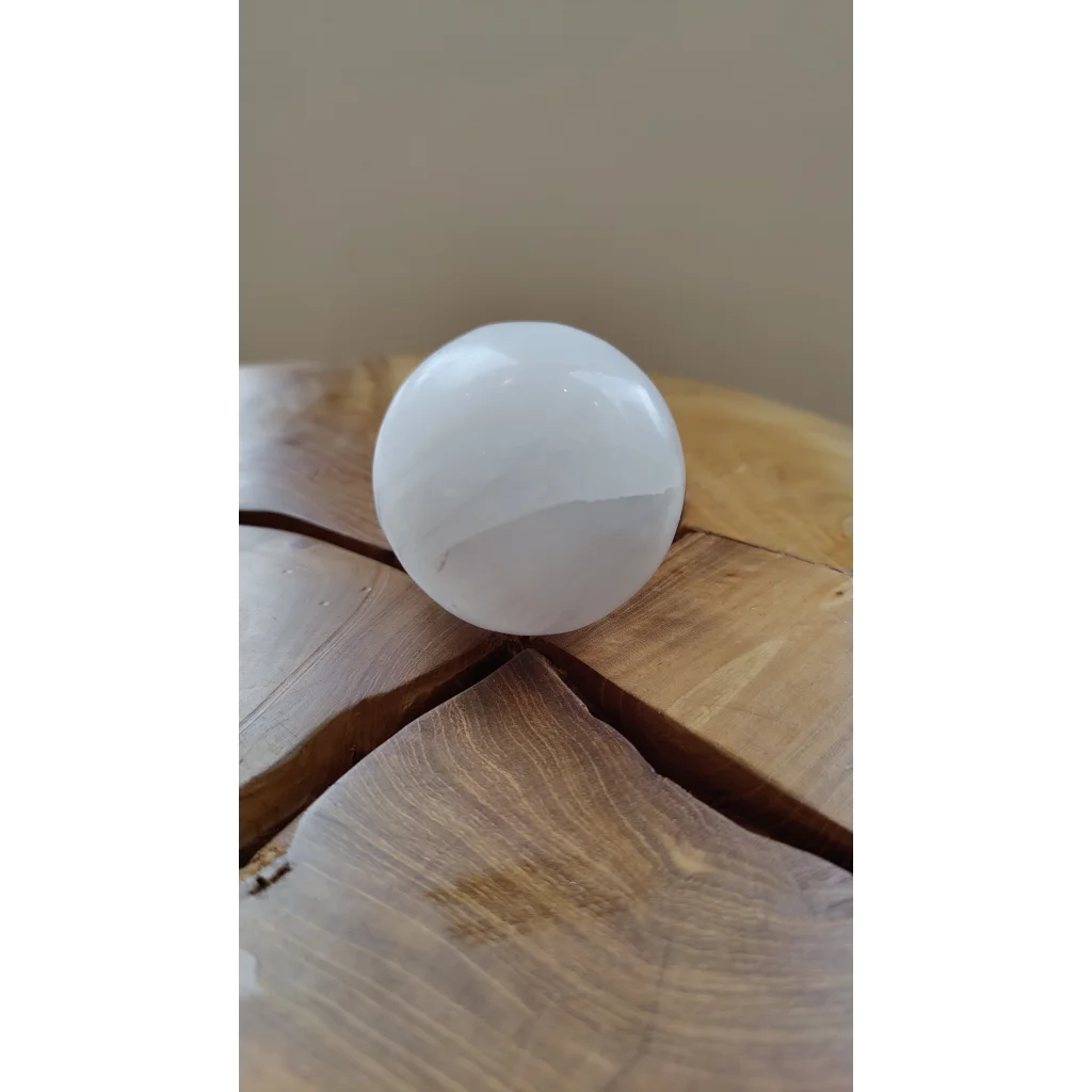 Smooth translucent selenite sphere on rustic wood for sacred space