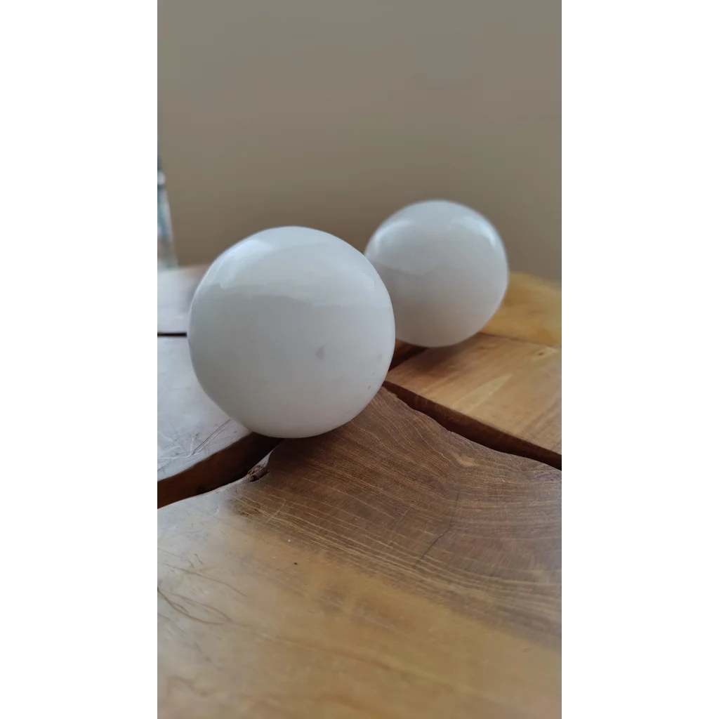 Two smooth white selenite spheres on rustic wood for sacred space