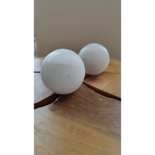 Two smooth white selenite spheres on rustic wood for sacred space