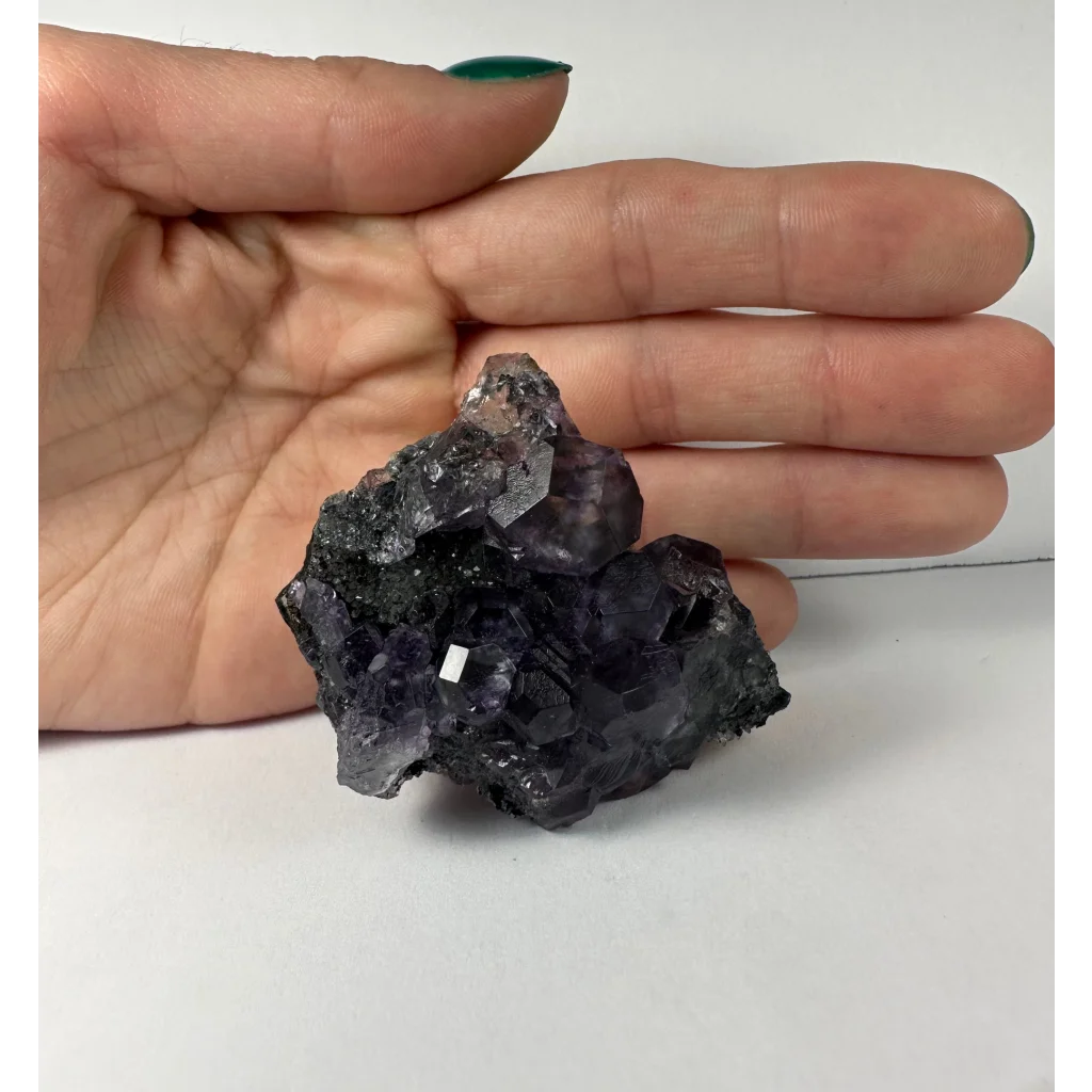 Hand holding stunning purple dodecahedral fluorite cluster from China