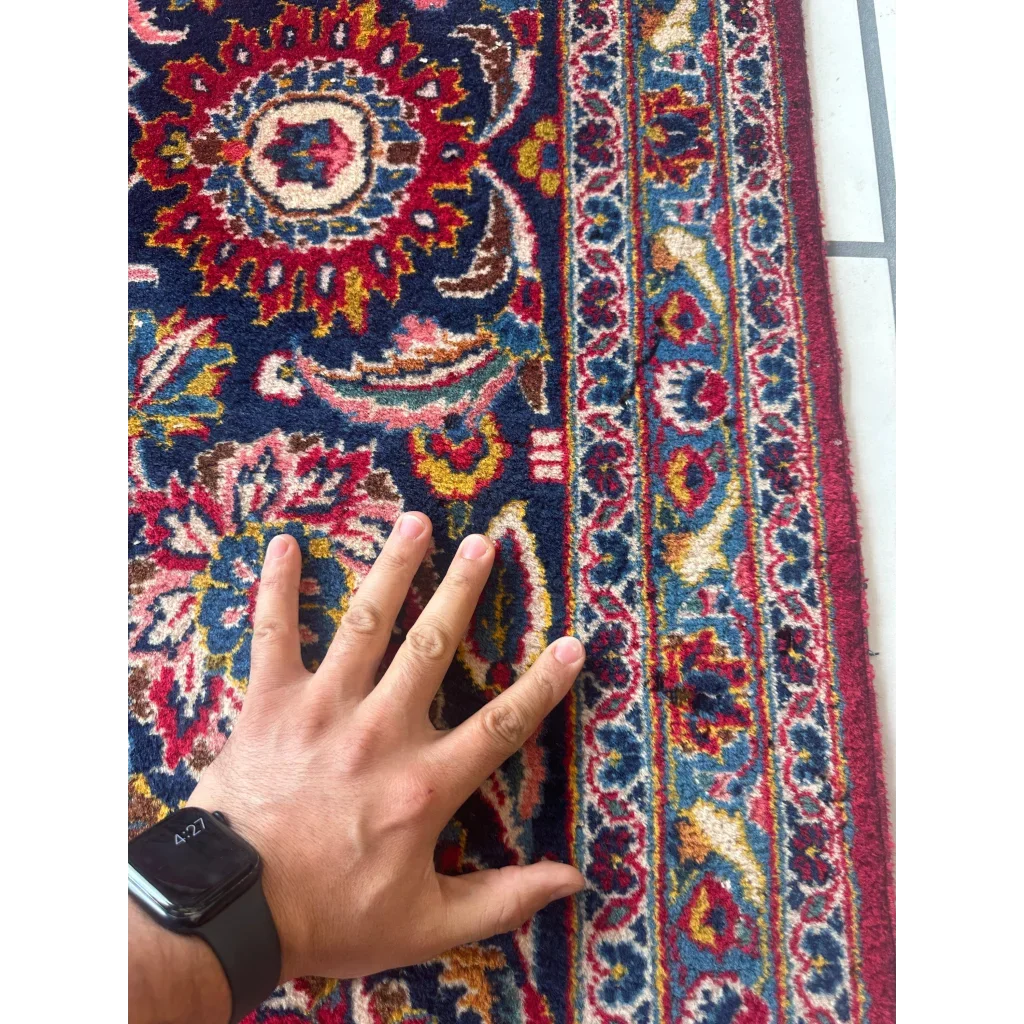 Hand on black Apple Watch rests on stunning red Persian rug with floral patterns