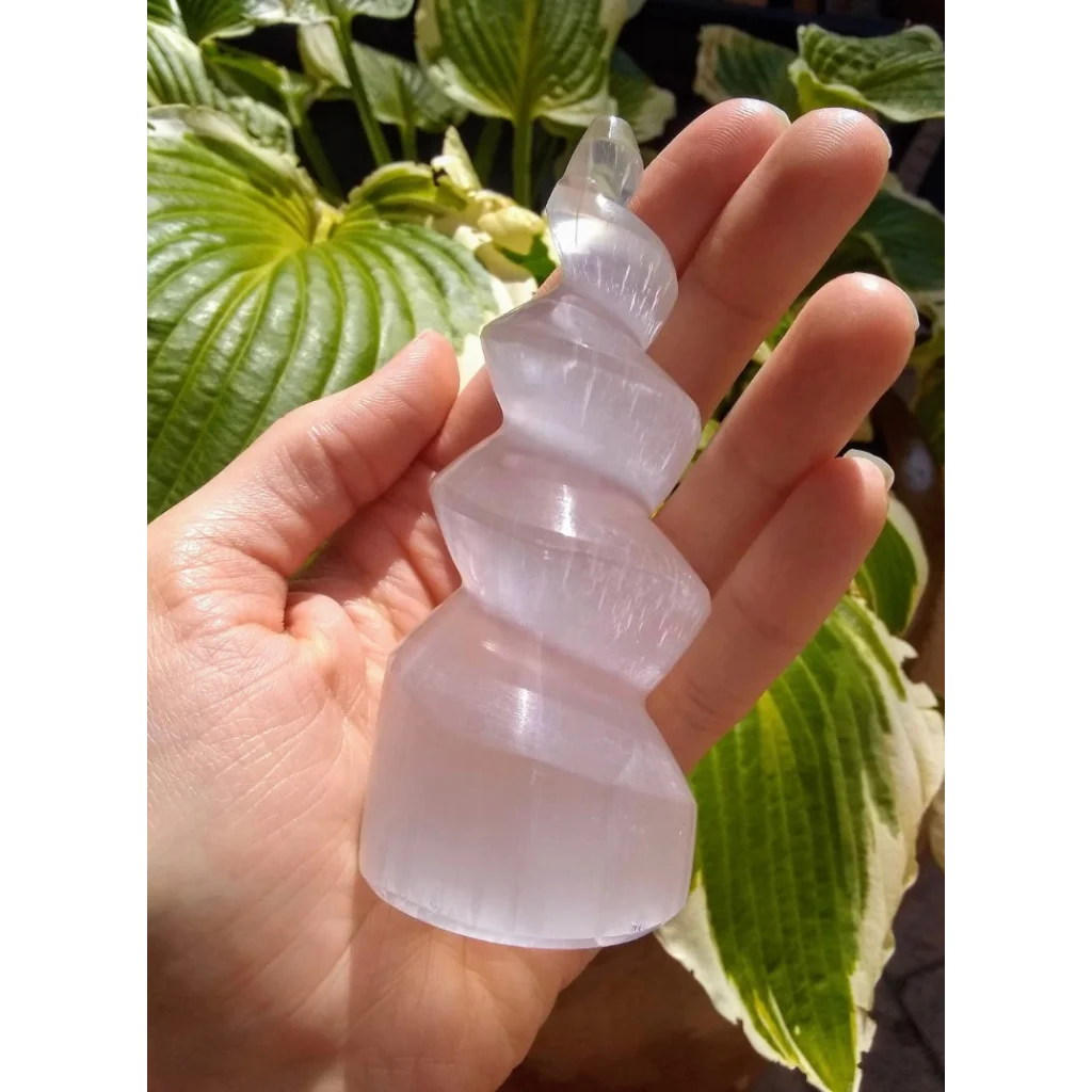 Hand holding translucent pale pink selenite spiral tower from Morocco
