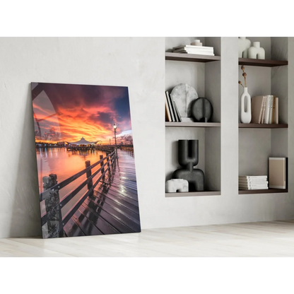 Vibrant sunset over water with wooden pier and city skyline glass wall art