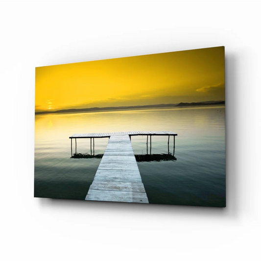 Stunning yellow sky over wooden pier on calm water glass wall art