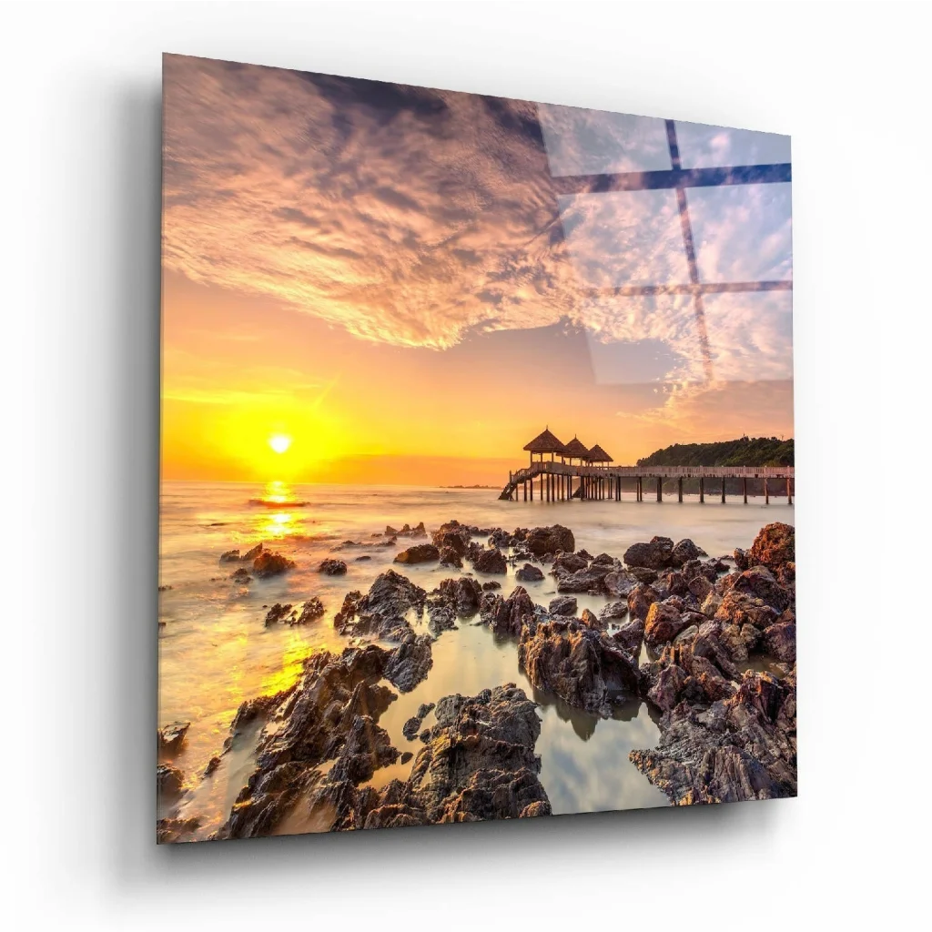 Vibrant sunset glass wall art over rocky shoreline with pier