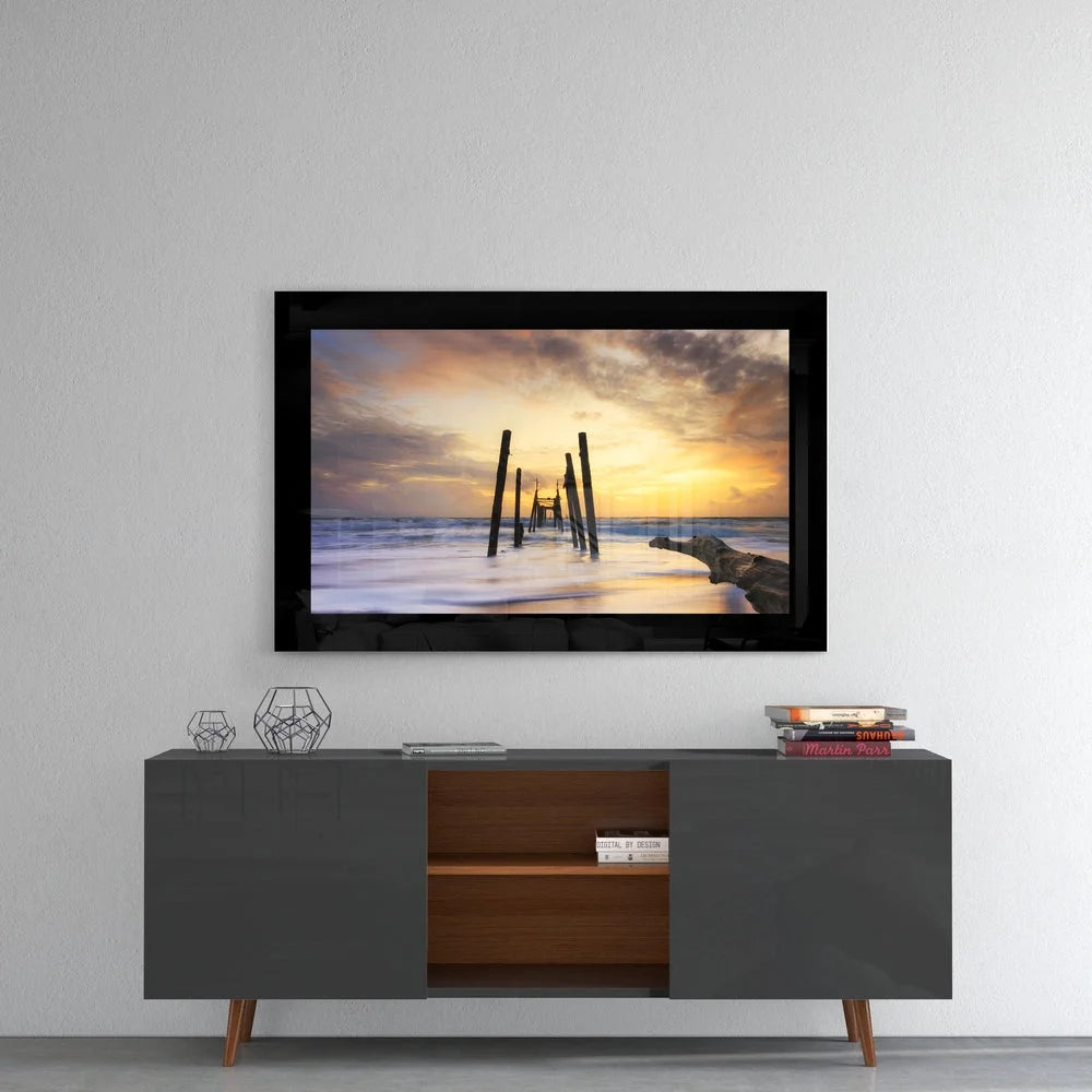 Stunning sunset over ocean pilings in black-framed glass wall art