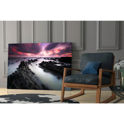 Vibrant coastal sunset glass wall art print with swirling purples, pinks, and oranges above rocks and water