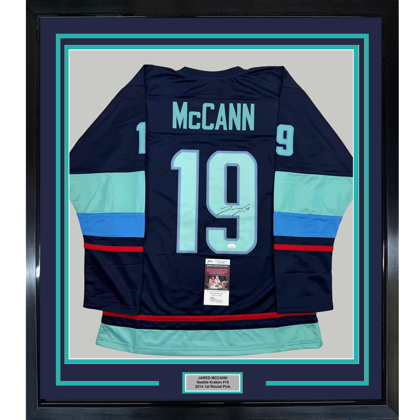 Framed navy Seattle Kraken hockey jersey #19 McCann displayed flat against light gray backing with turquoise border matting and JSA authentication certificate visible.