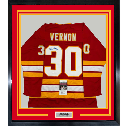 Framed red Calgary Flames hockey jersey #30 with "VERNON" nameplate, signed, displayed flat against gray backing with red and yellow matting.