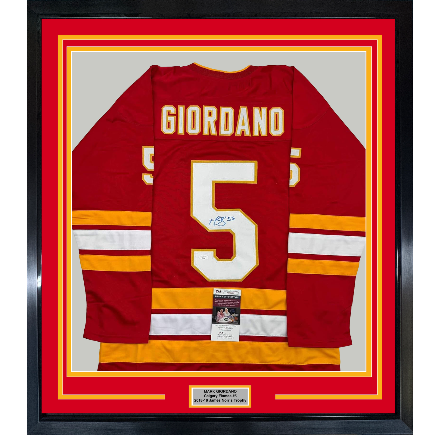 Framed red Calgary Flames hockey jersey number 5 with "GIORDANO" nameplate, signed in blue ink, displayed flat against gray background with yellow and red matting.
