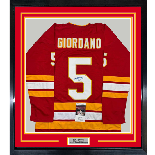 Framed red Calgary Flames hockey jersey number 5 with "GIORDANO" nameplate, signed in blue ink, displayed flat against gray background with yellow and red matting.