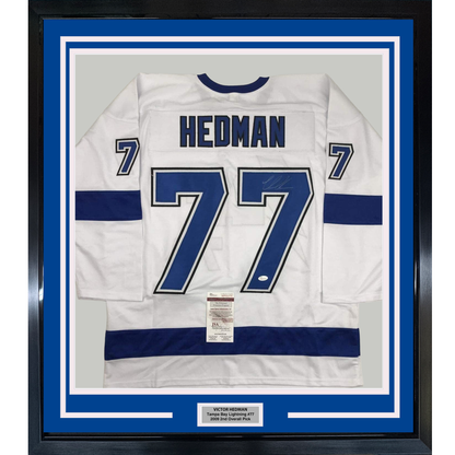 White Tampa Bay Lightning #77 hockey jersey with navy blue stripes framed behind glass with blue matting and authentication certificate.