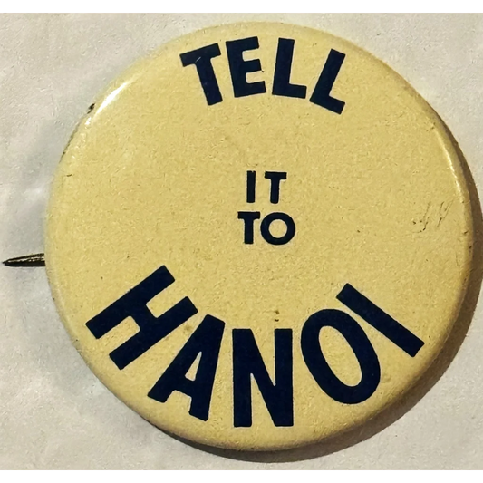 Circular yellow button with black text saying TELL IT TO HANOI from 1960s Vietnam War