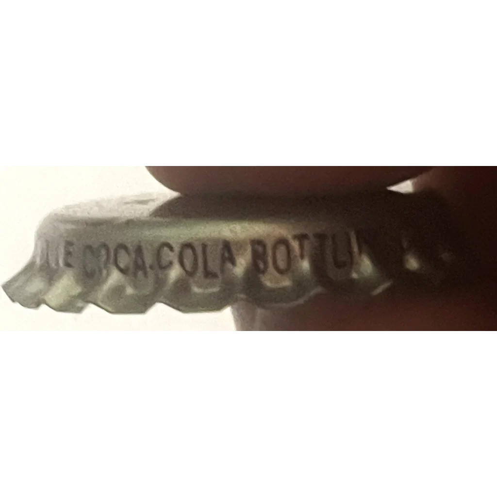 Blurred text on a curved surface showing Coca-Cola bottle cap from rare 1970s grape soda