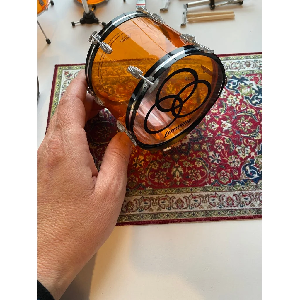 Orange drum head with black rim logo on vintage drum rug for scale drum kit