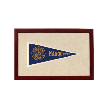 A navy blue vintage marquette university pennant with gold lettering and emblem in a wooden frame