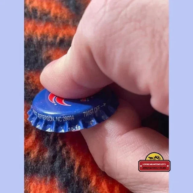 Blue bottle cap held between fingers, featuring Rare 90s Royal Crown Cola design